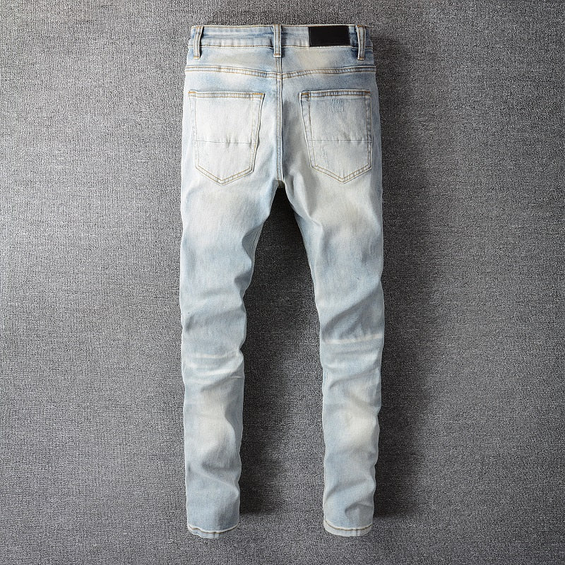 Men's light indigo skinny jeans with ripped holes, rhinestone accents, and distressed details for a stylish streetwear look